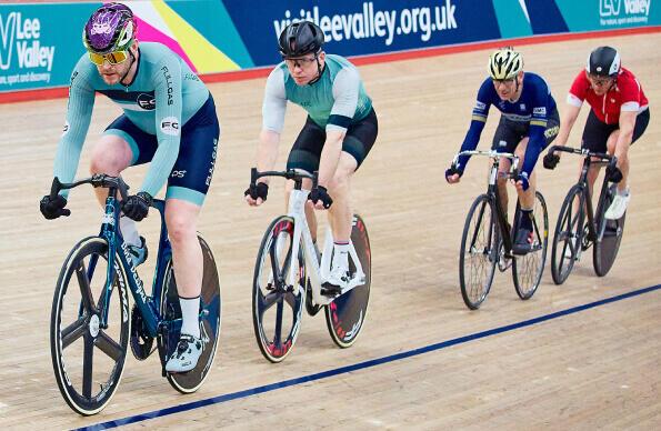 Four people ride bikes round the velodrome