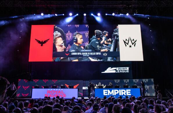 A crowd watches a big screen as players compete at e-sports