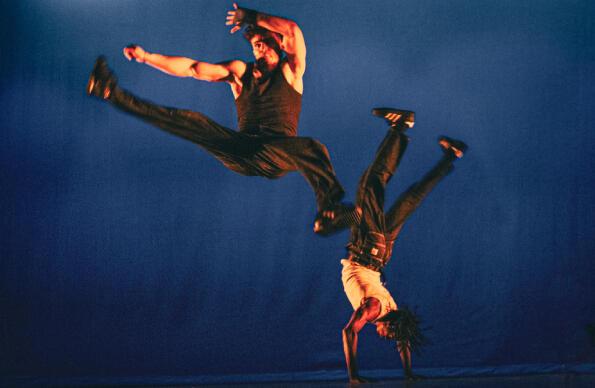 Two dancers on stage, one in a handstage, one jumping