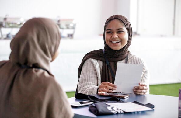 Woman with hijab talks over a table to friend