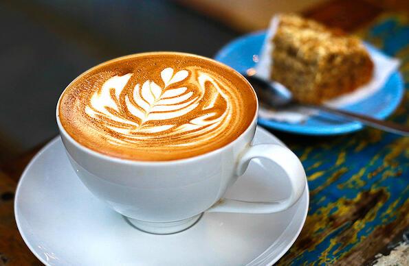 A shot of a coffee with latte art and cake