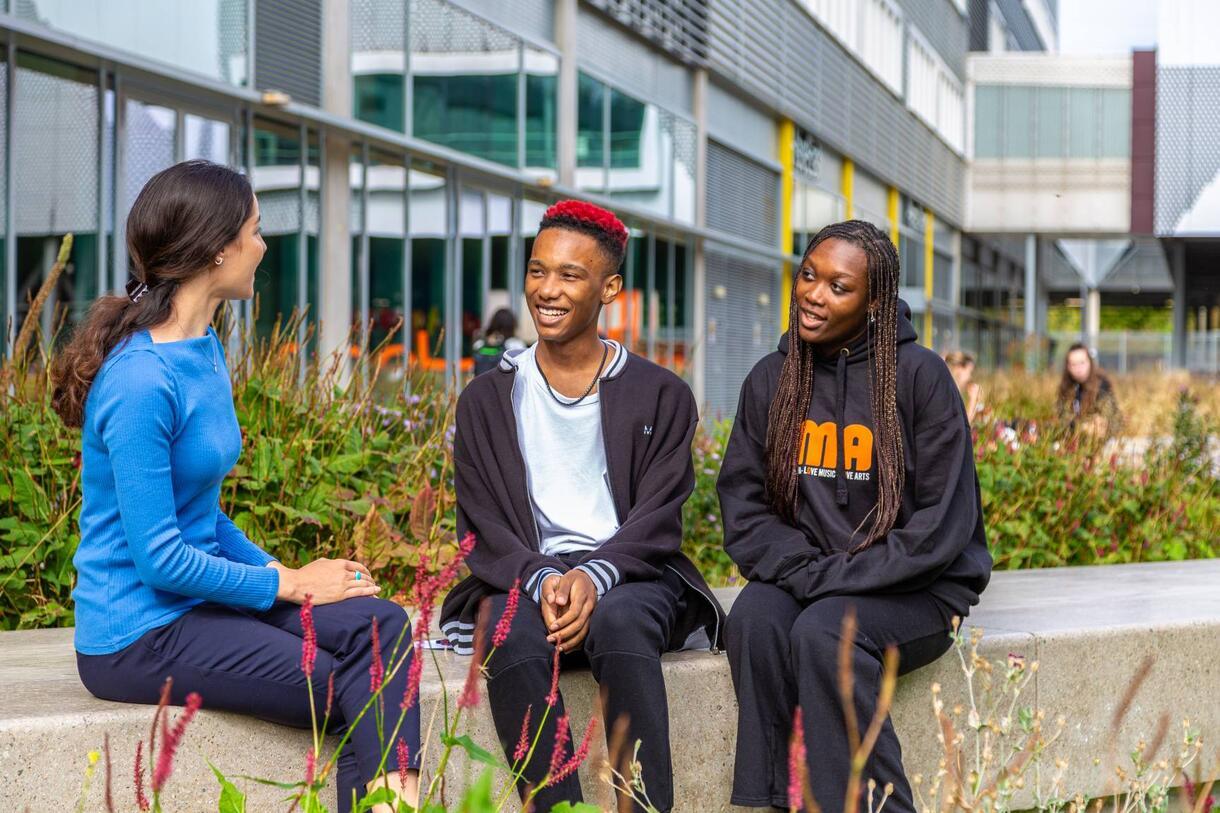 Three people sitting on a bench at Here East