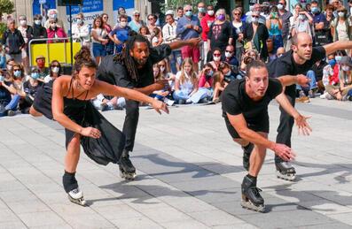 A group of dancers on rollerblades perform to a crowd outside