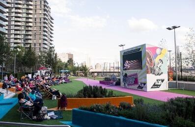 A crowd watches a sports match on an outside screen