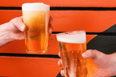 Two hands holding a beer in front of an orange background